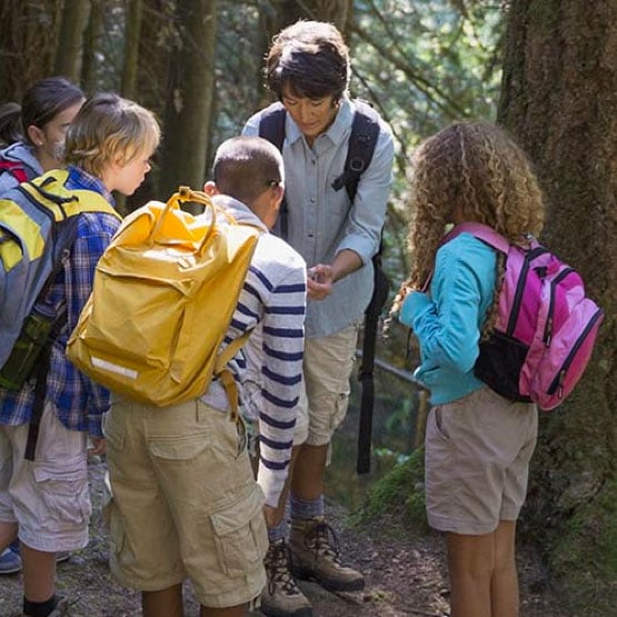 Our Impact Photo: Teacher in the woods educating four STEM students on ecology