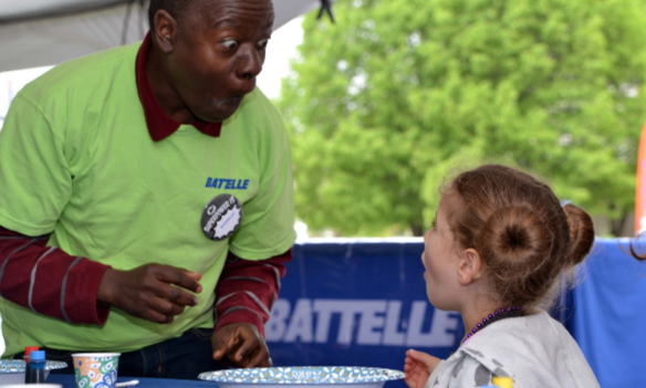 alt= battelle volunteer conducting an experiment with a little girl at the cosi science festival