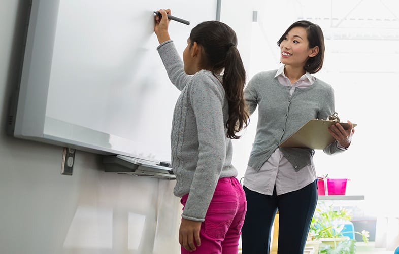 alt=a teacher helping a young girl with schoolwork on a whiteboard