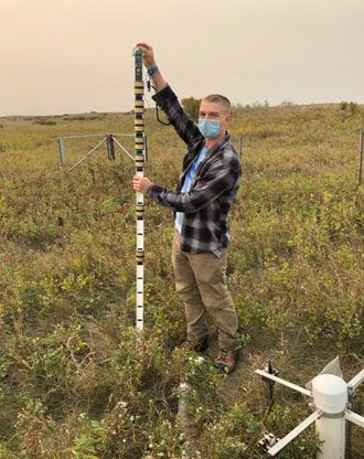 Photo: Senior Neon Technician inserting a soil moisture sensor into a soil plot.