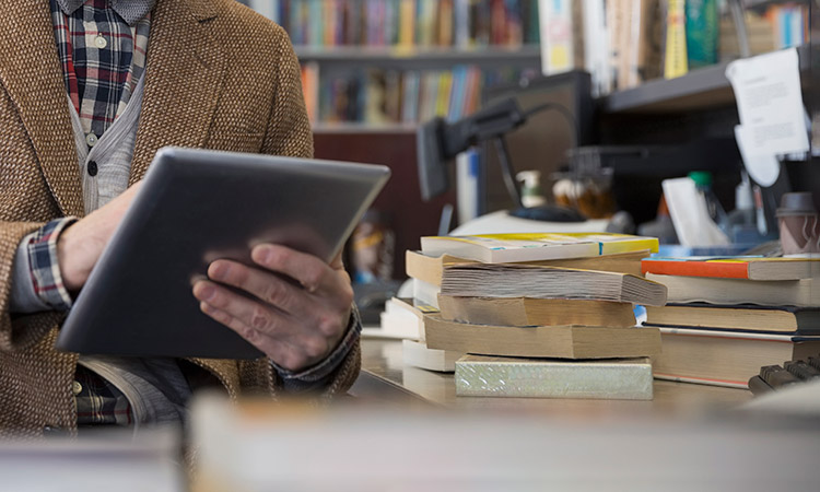 Photo: Individual using a tablet next to books
