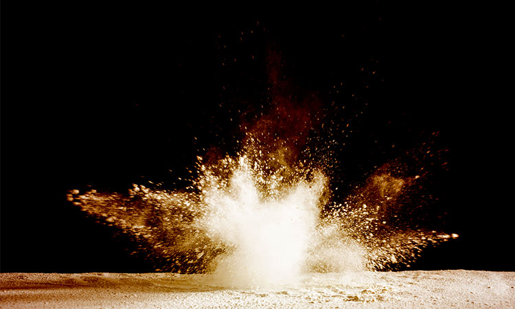 Photo: explosion in sand in front of a black background