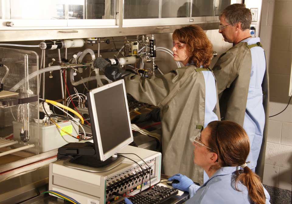 Photo: Scientists in protective suits examining equipment at Hazardous Materials Research Center